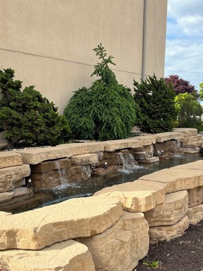 Un élément décoratif aquatique bordé de rochers, avec de l’eau en cascade, entouré de divers arbustes et plantes.