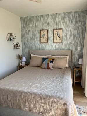 Un dormitorio con una cama grande, dos cuadros de pájaros colgados en la pared y un papel tapiz con textura.