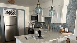Una cocina moderna con armarios blancos, un refrigerador de acero inoxidable, un microondas y una isla grande con taburetes de bar.