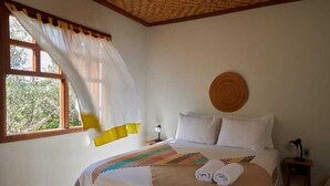 A bedroom with a bed, a window with curtains, a bedside table, and a round wall decoration. - Pousada do Pequi (Serro)