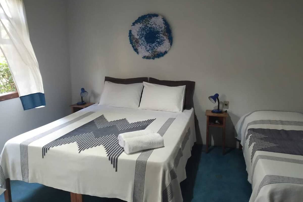A bedroom with a bed, two bedside tables, a wall decoration, and a window with curtains.