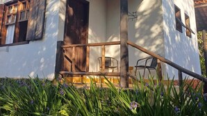 A white building with a tiled roof, a wooden door, and a small porch with a chair. - Pousada do Pequi (Serro)
