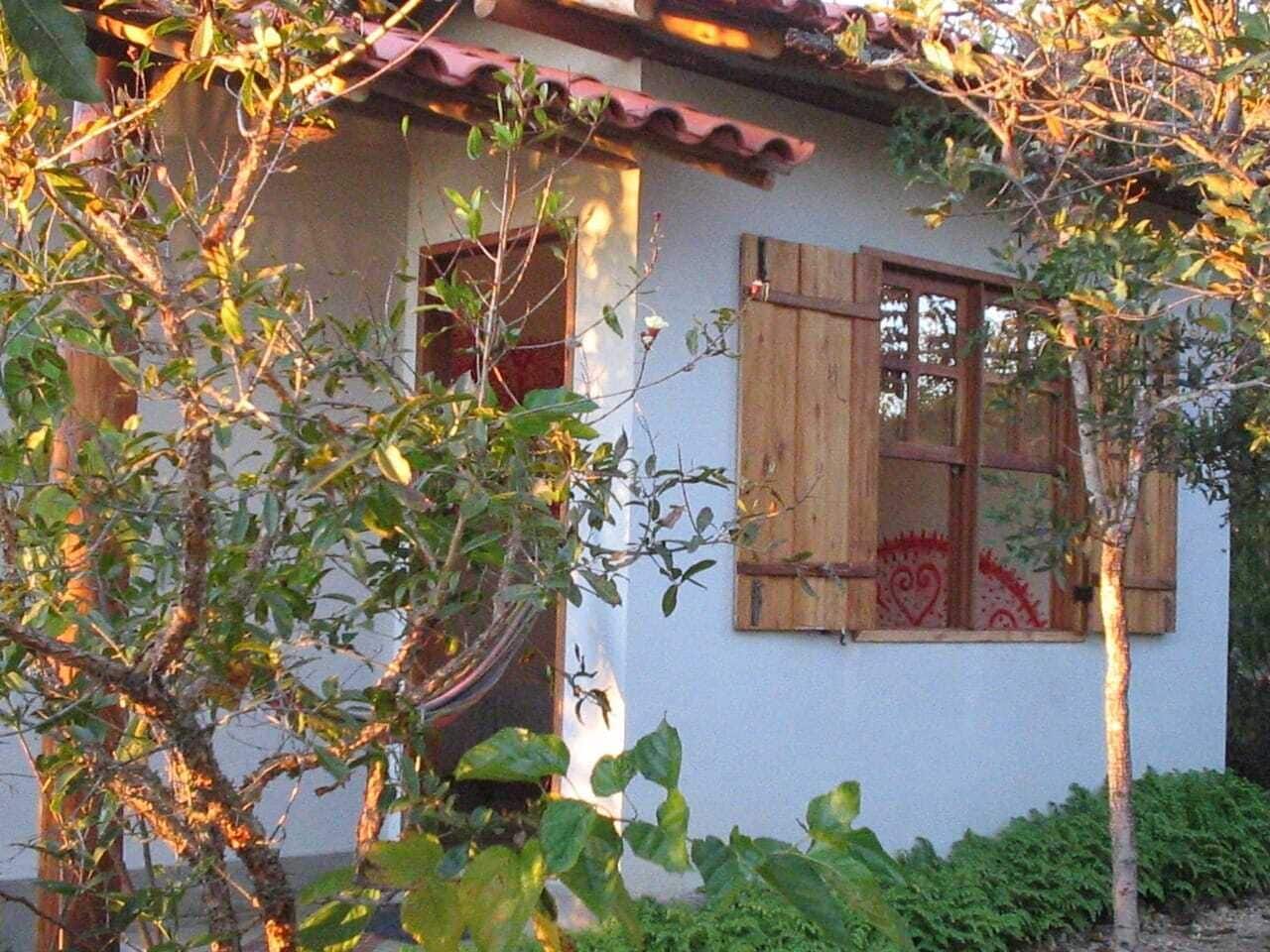 A house with a white exterior, a red-tiled roof, and a window with a wooden shutter.