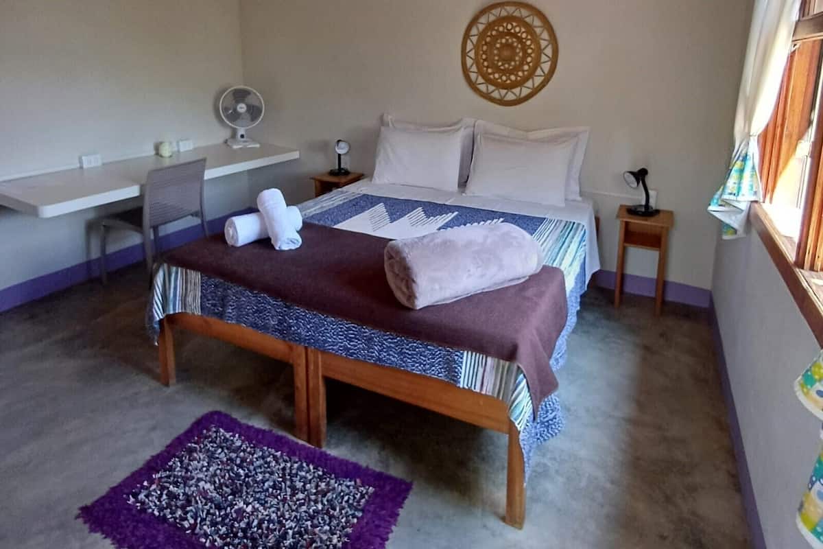 A bedroom with a bed, bedside tables, a desk, a hanging light, and a decorative wall piece.