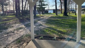 Un espace extérieur abrité, doté d’un sol en béton, entouré d’arbres et offrant une vue sur un lac.