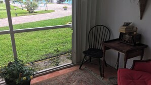 A room with a large window, a chair, a small table with a radio, and a red chair.