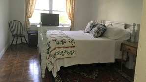 A bedroom with a bed, a chair, a television, and a window with curtains.