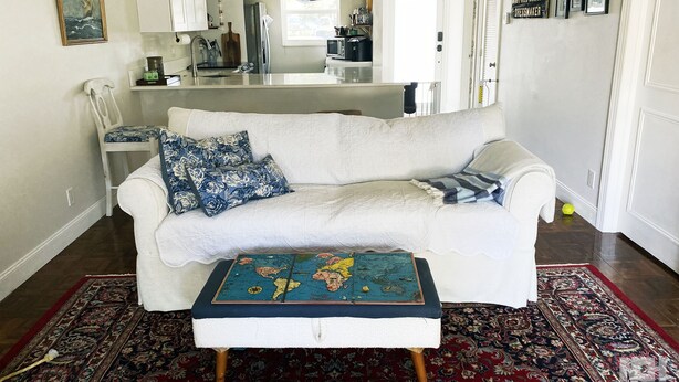 A living room with a white sofa, a matching ottoman, a patterned rug, and a world map on the ottoman.