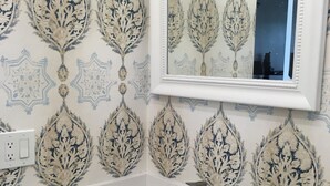 A bathroom with a white sink, a mirror, and patterned wallpaper.