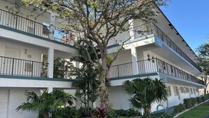 A multi-story hotel with balconies, a large tree in the center, and well-maintained landscaping.