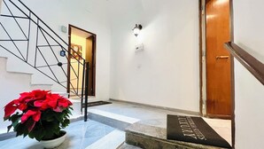 A staircase with a black handrail, a potted plant with red flowers, and a wooden door. - PRETORIA SUITES (Palermo)