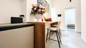 A modern kitchen with a wooden counter, a white vase with flowers, a fruit bowl, and a painting on the wall. - PRETORIA SUITES (Palermo)
