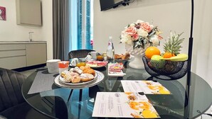 A modern hotel room with a dining table set for breakfast, a flower vase, and a fruit bowl. - PRETORIA SUITES (Palermo)