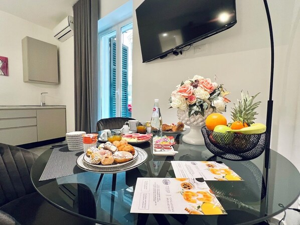 A modern hotel room with a dining table set for breakfast, a flower vase, and a fruit bowl.