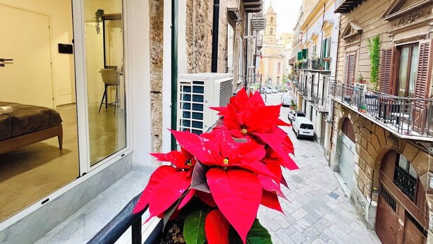 A narrow street with a balcony, a potted plant, and a building with a visible door and window. - PRETORIA SUITES (Palermo)