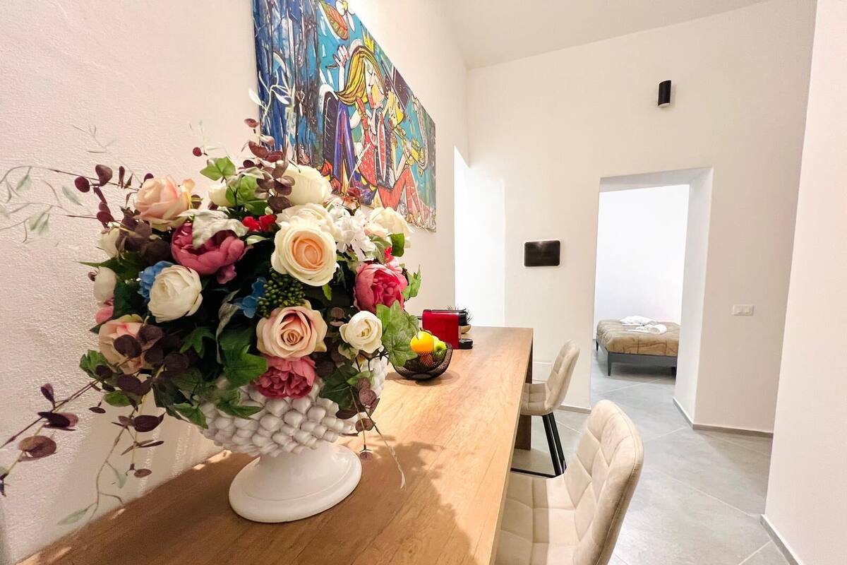 Et spiseområde med et træbord, en hvid blomsterdekoration og et farverigt billede på væggen.