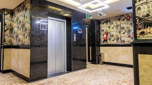 A lobby with a marble floor, a modern elevator, and a wall with a cityscape mural. - Dan Pelatenium (Madinah)