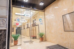 A hotel entrance with a glass door, a reception desk, and a potted plant.