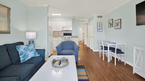 A modern living room with a sofa, coffee table, and a dining area with chairs and a table. - Cozy 1-bedroom condo in adorable Tybee Island (Tybee Island)