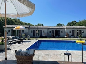 A swimming pool with a patio area, outdoor furniture, and a building with multiple doors and windows.