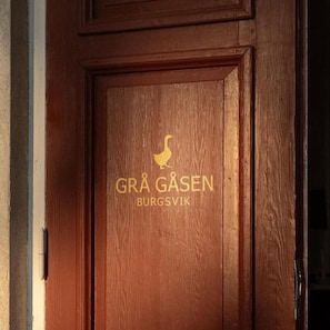 A wooden door with the text 'GRÅ GÅSEN BURGSVIK' and a stylized bird logo. - Boutiquehotell Grå Gåsen (Burgsvik)