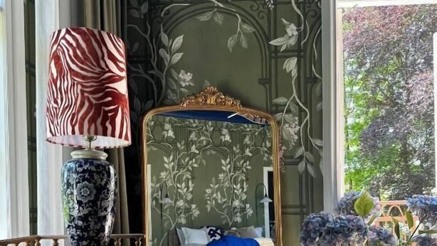 Un dormitorio con cama, espejo, lámpara, mesa y un amplio ventanal.