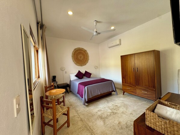 A bedroom with a bed, a wooden wardrobe, a ceiling fan, and a small table with chairs.