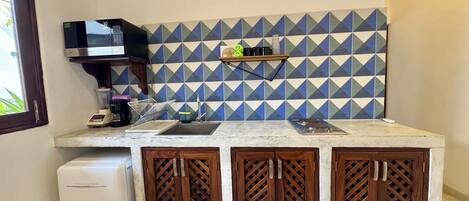 A compact kitchen with a microwave, blender, and sink. It features a geometric tile backsplash and wooden cabinets.