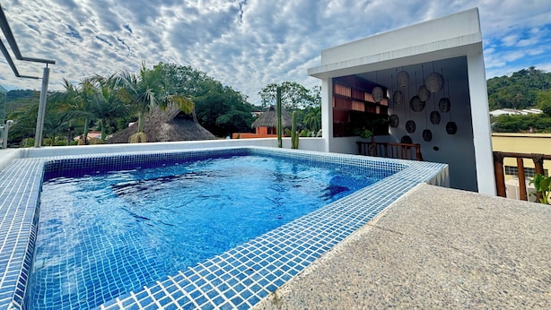 Una piscina con baldosas azules, rodeada por un edificio blanco con un balcón y adornos colgantes.