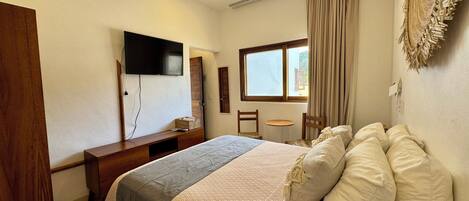 A bedroom with a bed, a desk, a chair, a television, a window, and a ceiling fan.