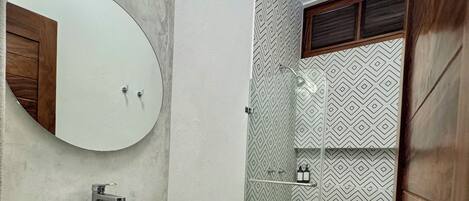 Un baño con lavamanos blanco, espejo, inodoro y zona de ducha.