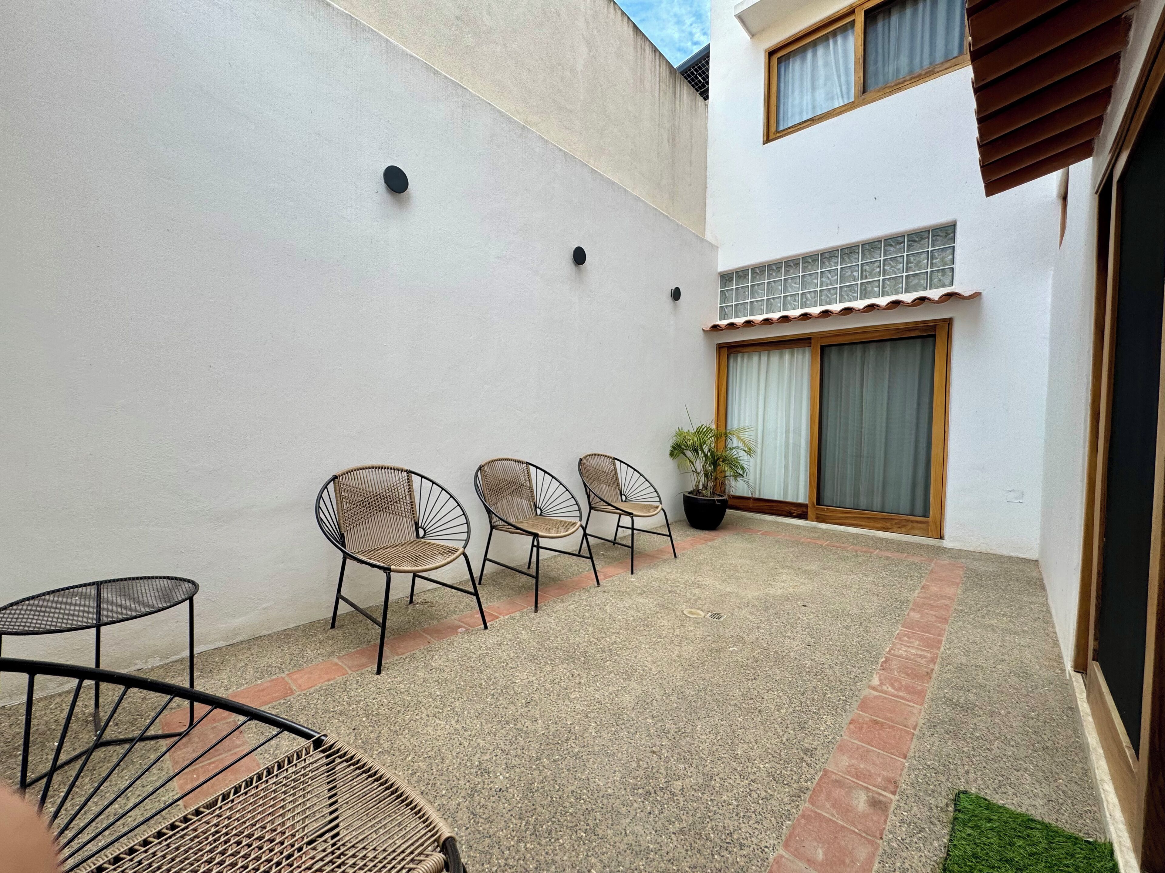 A small outdoor patio area with three wicker chairs, a small round table, and a potted plant.