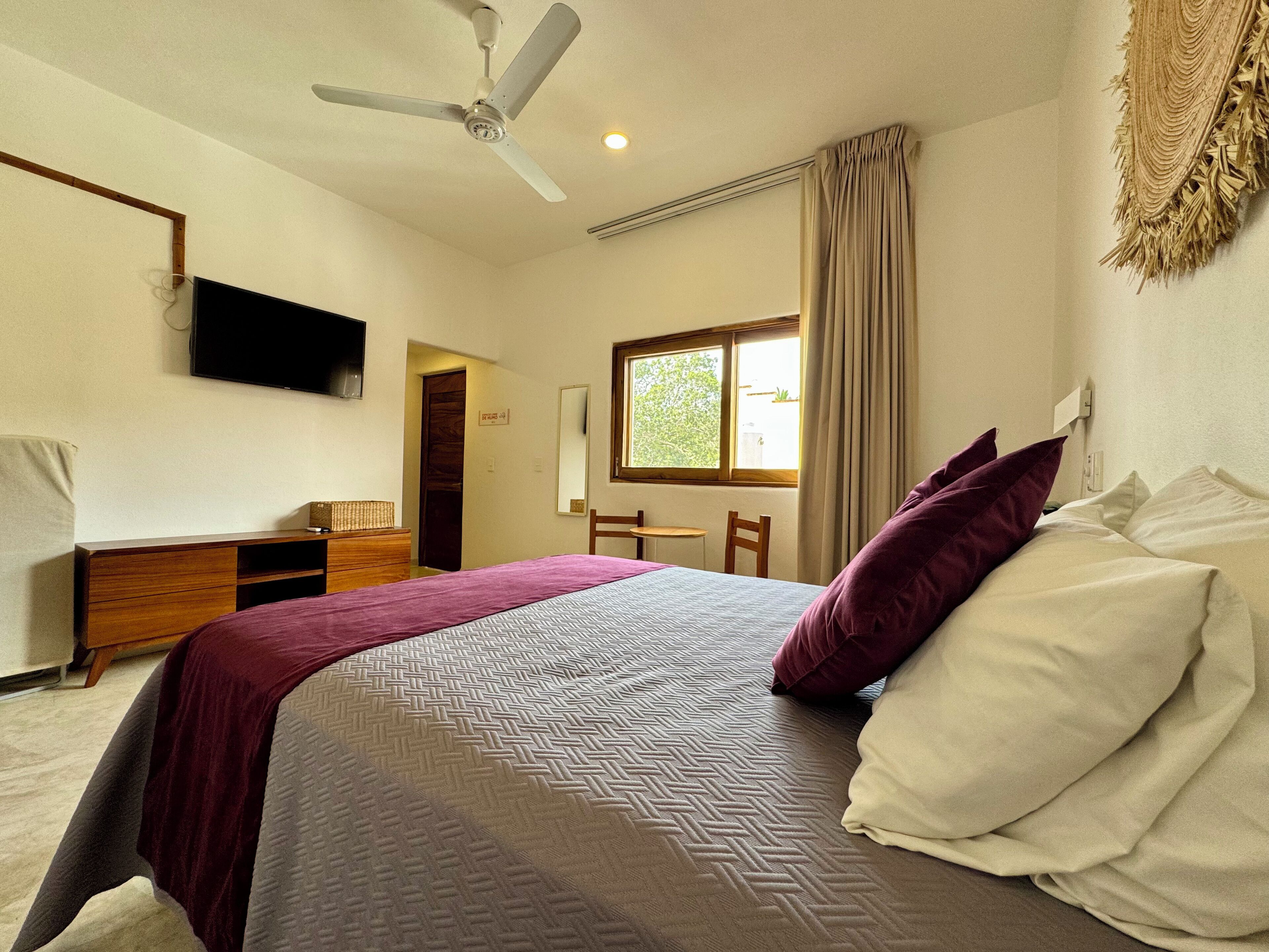 A bedroom with a bed, a desk, a chair, a television, and a ceiling fan.