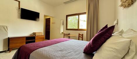 A bedroom with a bed, a desk, a chair, a television, and a ceiling fan.