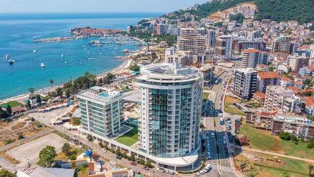 Ein Hochhaus-Hotel mit moderner Glasfassade, gelegen in Küstenähe mit einem Yachthafen.