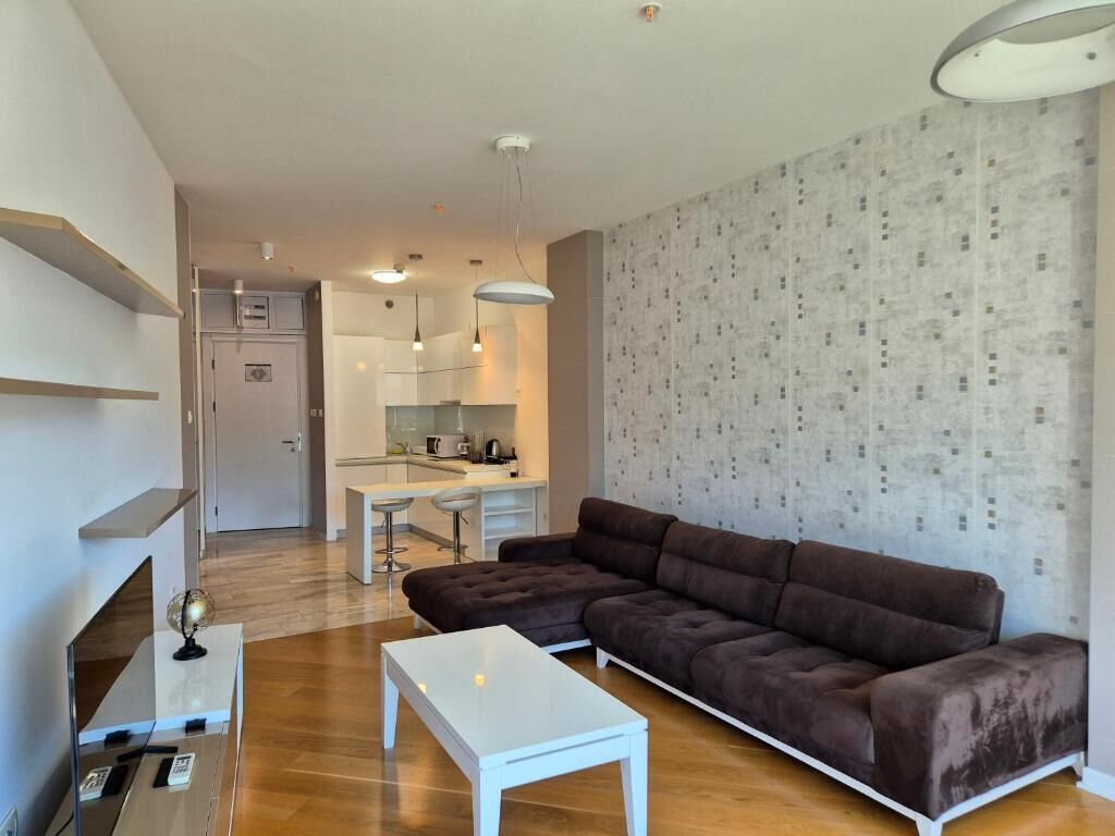 Ein modernes Wohnzimmer mit einer Eckcouch, einem weißen Couchtisch und einer Küche im Hintergrund.