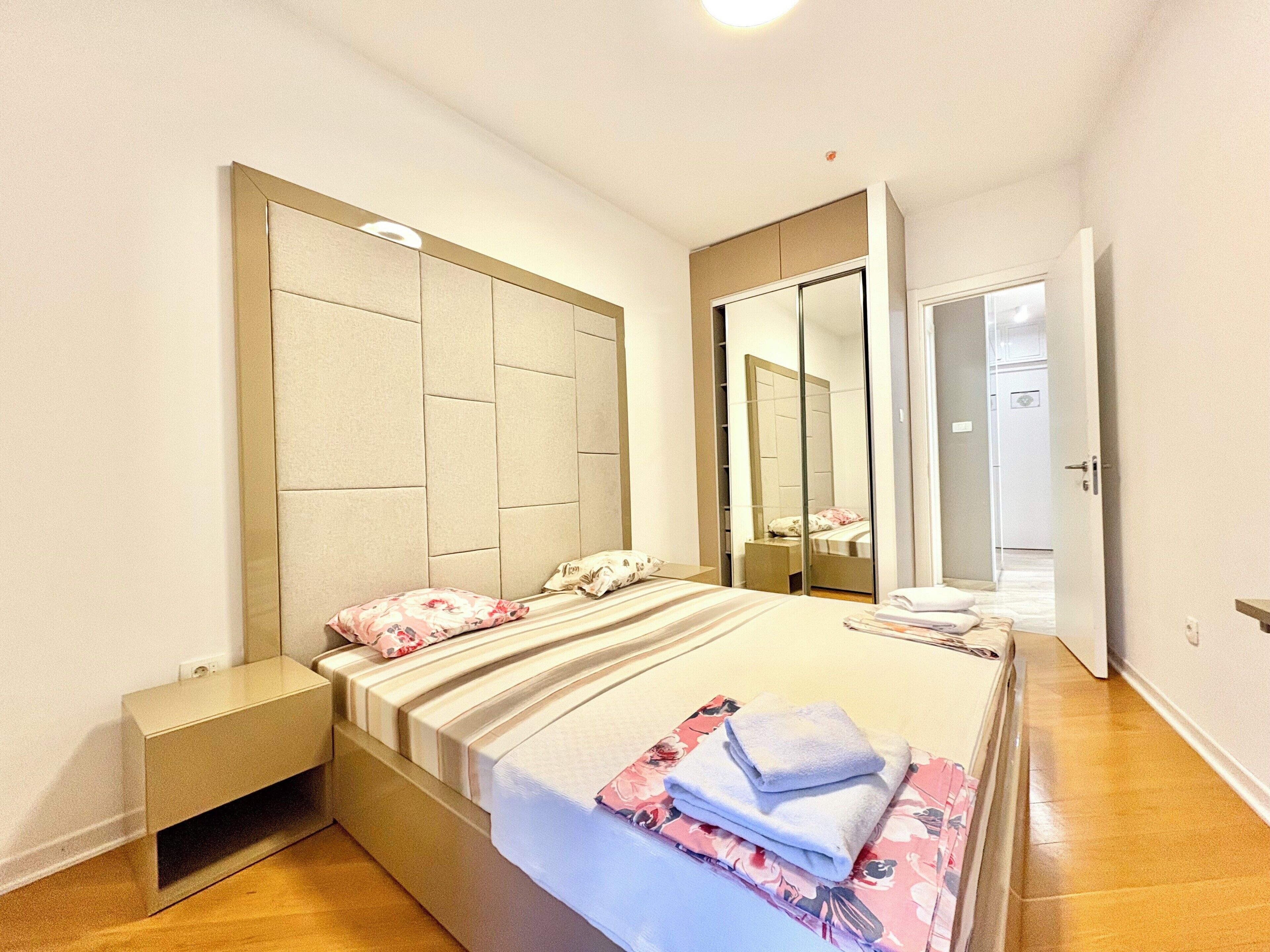 A bedroom with a bed, a nightstand, a mirror, and a door.