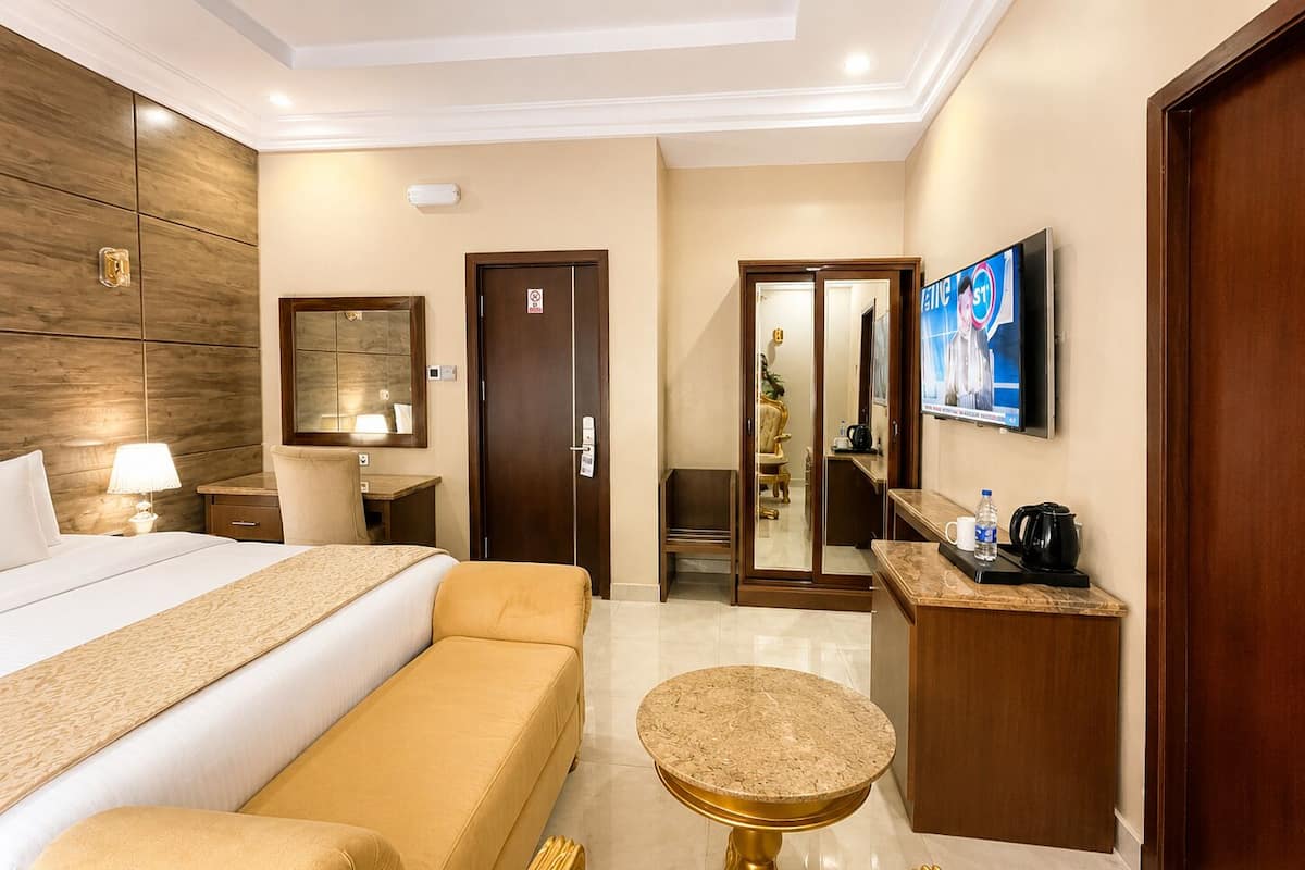 A hotel room with a bed, a sofa, a small round table, a desk, a television, and a mirror.