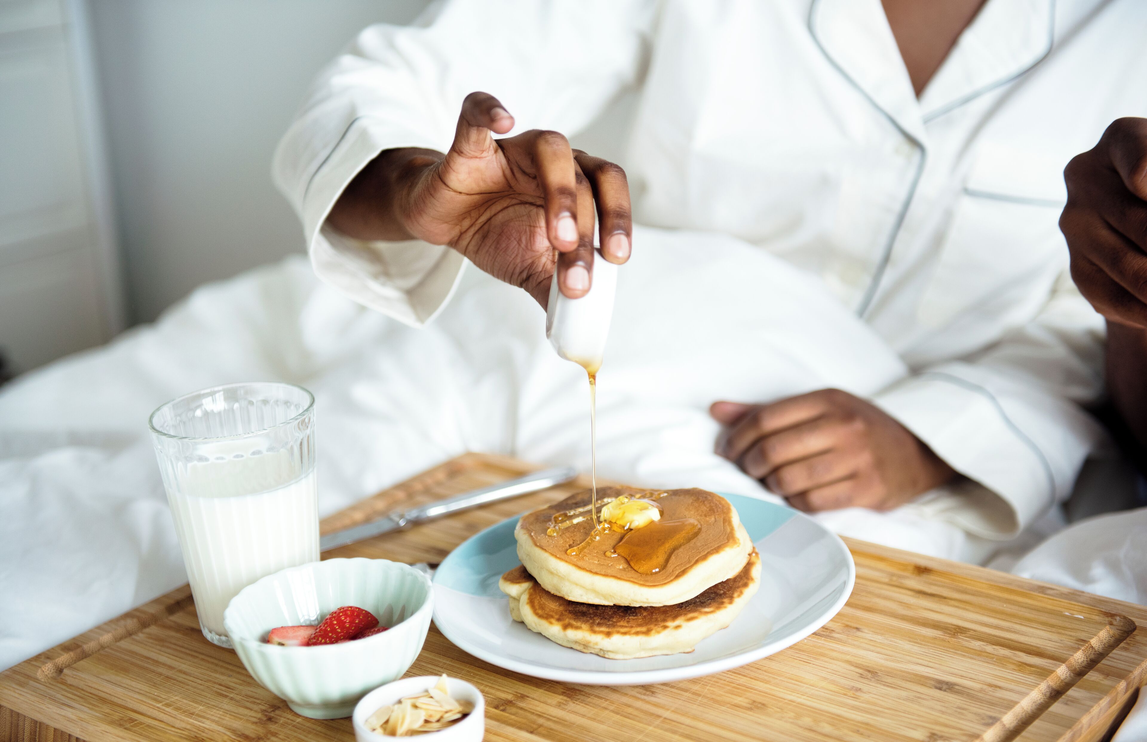 Une table en bois dressée pour le petit-déjeuner, avec des crêpes, du sirop, des fraises et du lait.