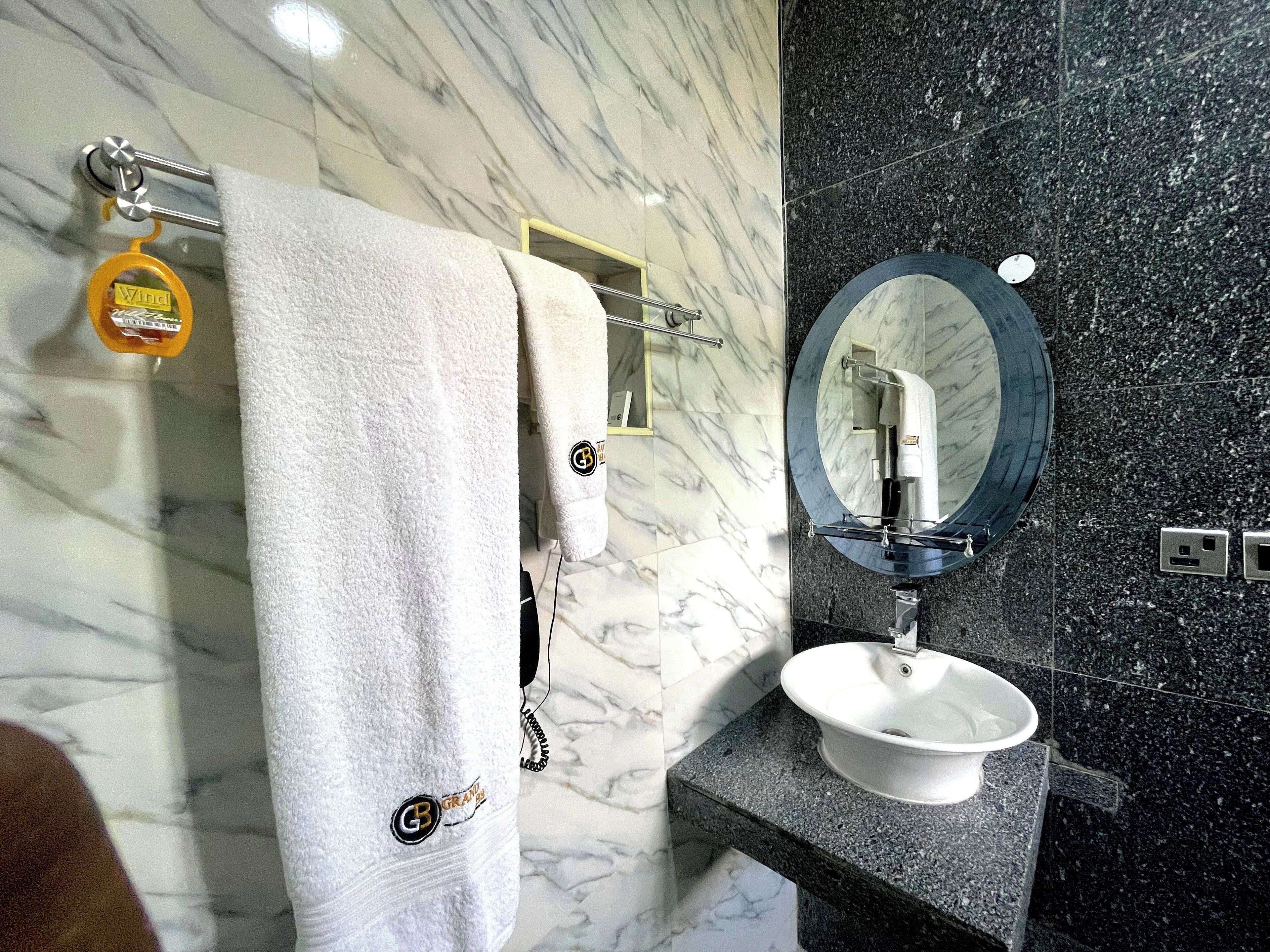Un baño con pared de mármol, una toalla blanca, un espejo redondo y un lavabo.