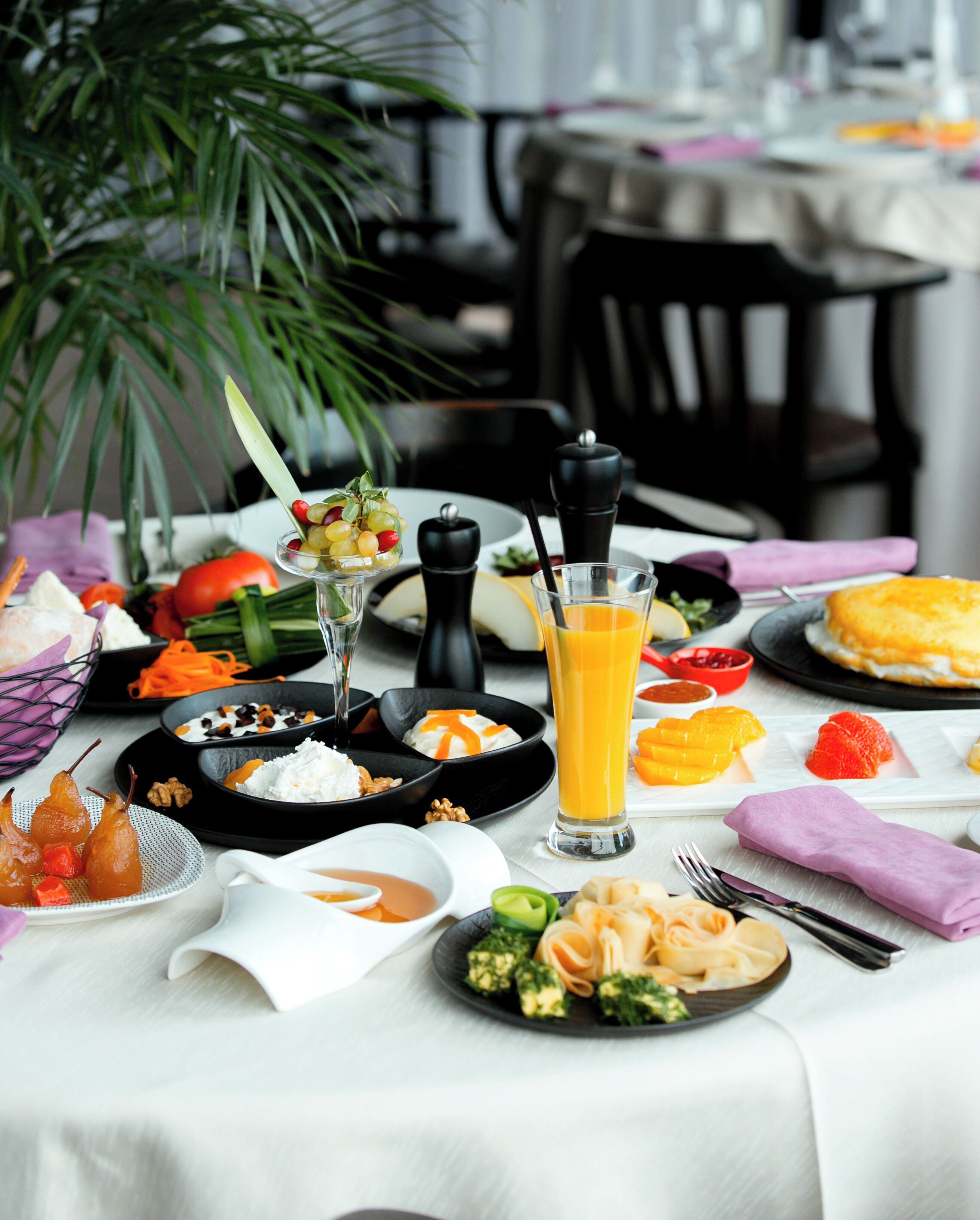 A table set with various dishes, including fruits, vegetables, and a glass of orange juice.