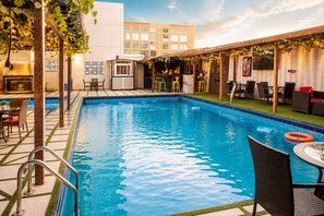A swimming pool with a bar area, outdoor seating, and a building in the background.