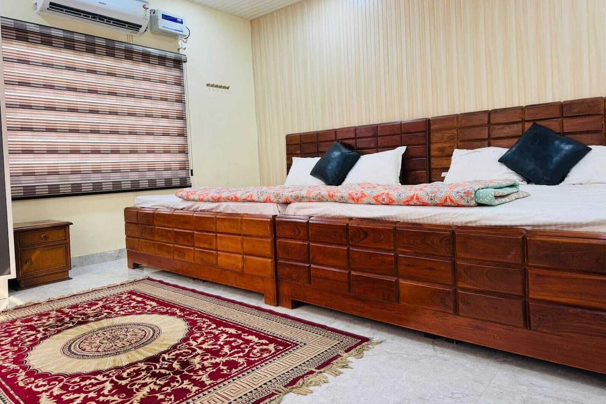 A bedroom with a wooden bed, a red and beige patterned rug, and an air conditioning unit on the wall.