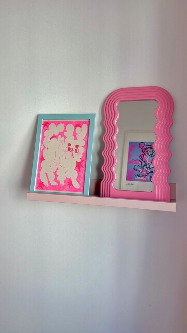 A wall-mounted shelf with two framed artworks and a pink-framed mirror.