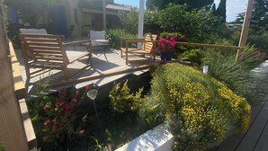 A covered patio with wooden furniture, a potted plant with pink flowers, and yellow flowers. - 140 M2 architect-designed house in a quiet cul-de-sac. (Vaison la romaine)