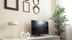 Ein modernes Wohnzimmer mit einem weißen Konsolentisch, einem Flachbildfernseher, zwei weißen Vasen, einer Stehlampe und einer Topfpflanze.