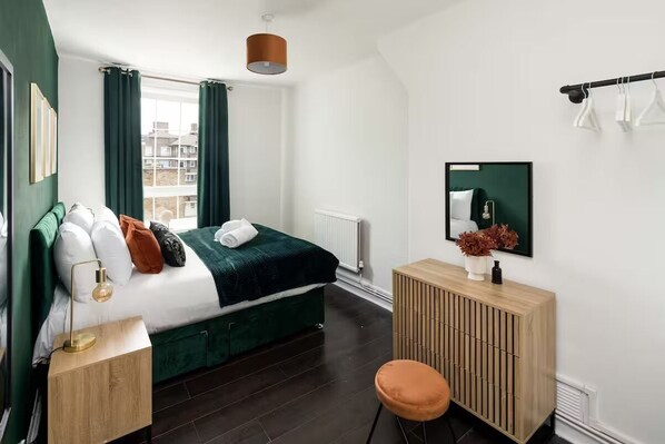 Een moderne slaapkamer met een met groen bekleden bed, een houten nachtkastje, een spiegel en een radiator.