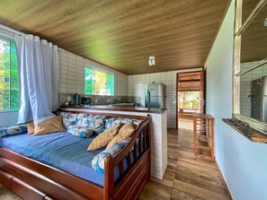 Une chambre avec un lit en bois, une petite kitchenette et une salle de bain visible à travers une porte ouverte.