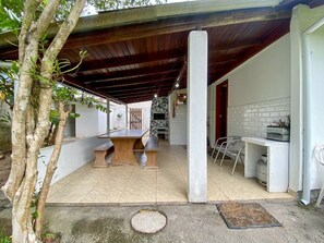 Une terrasse extérieure avec une table et des bancs en bois, une colonne blanche et un espace barbecue.