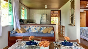 Un rincón acogedor con sofá, mesa de comedor para dos personas y cocina al fondo.